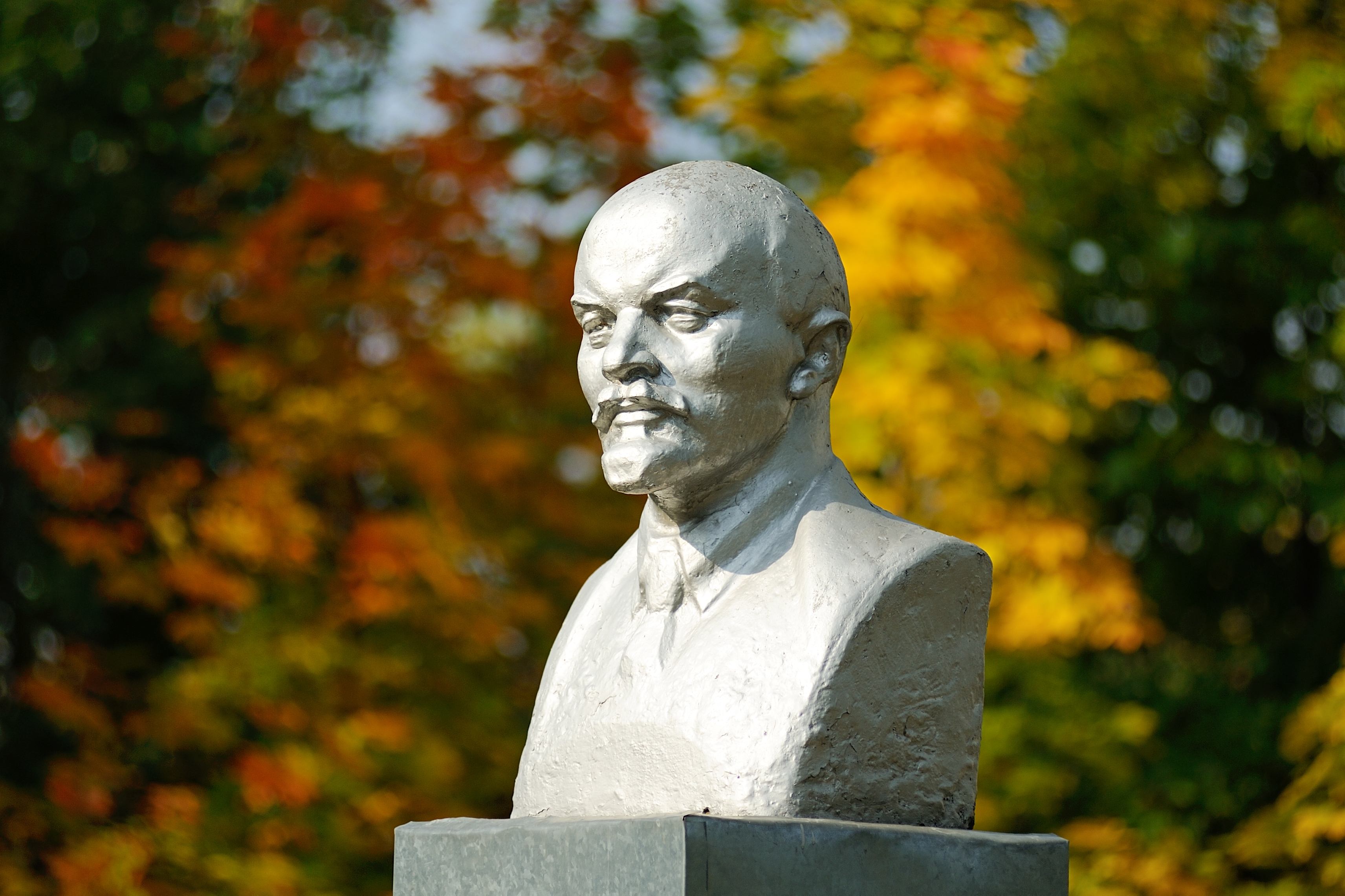 Lenin bust monument with autunm leaves on the background horizontal