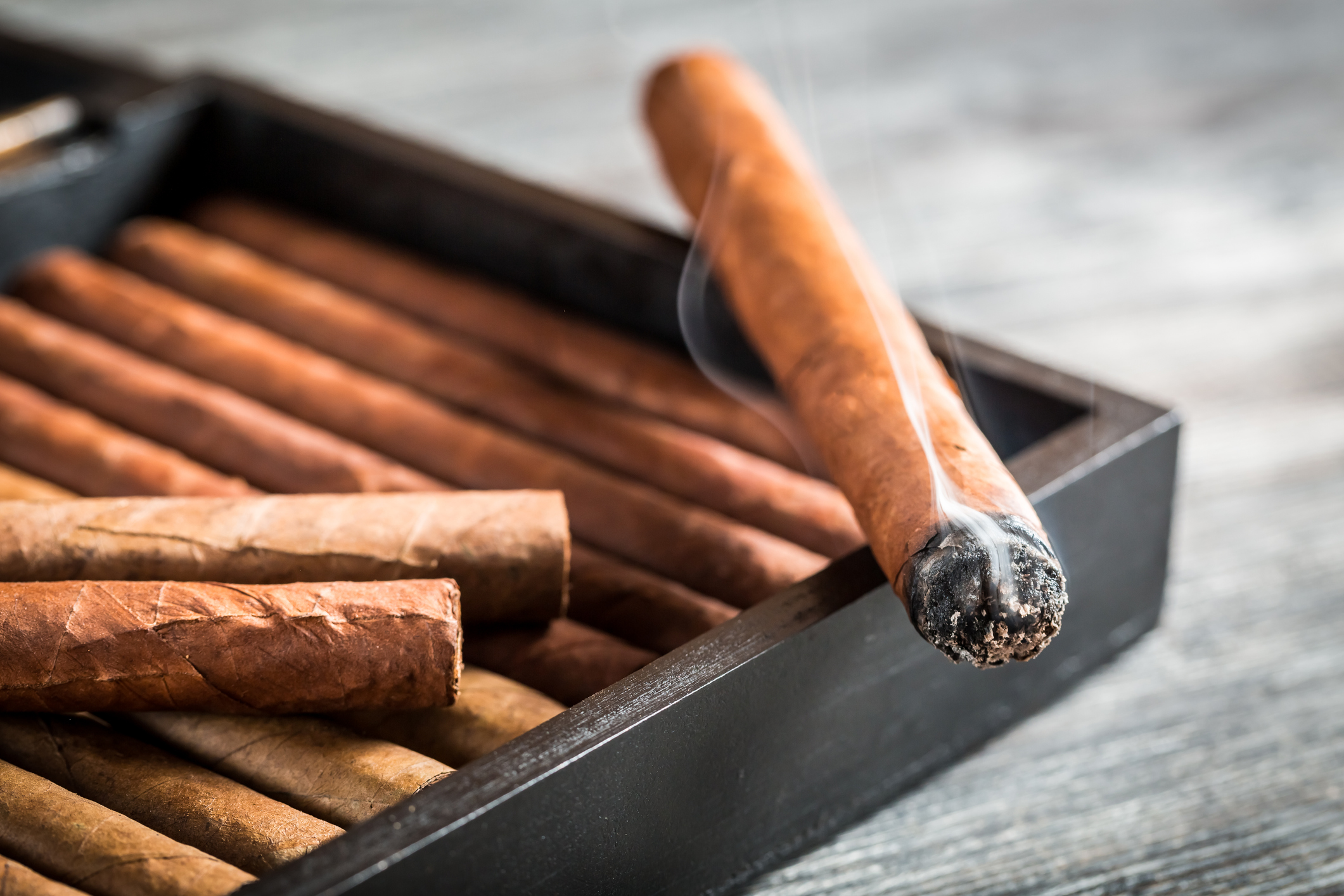 Burning cigar with smoke on wooden humidor